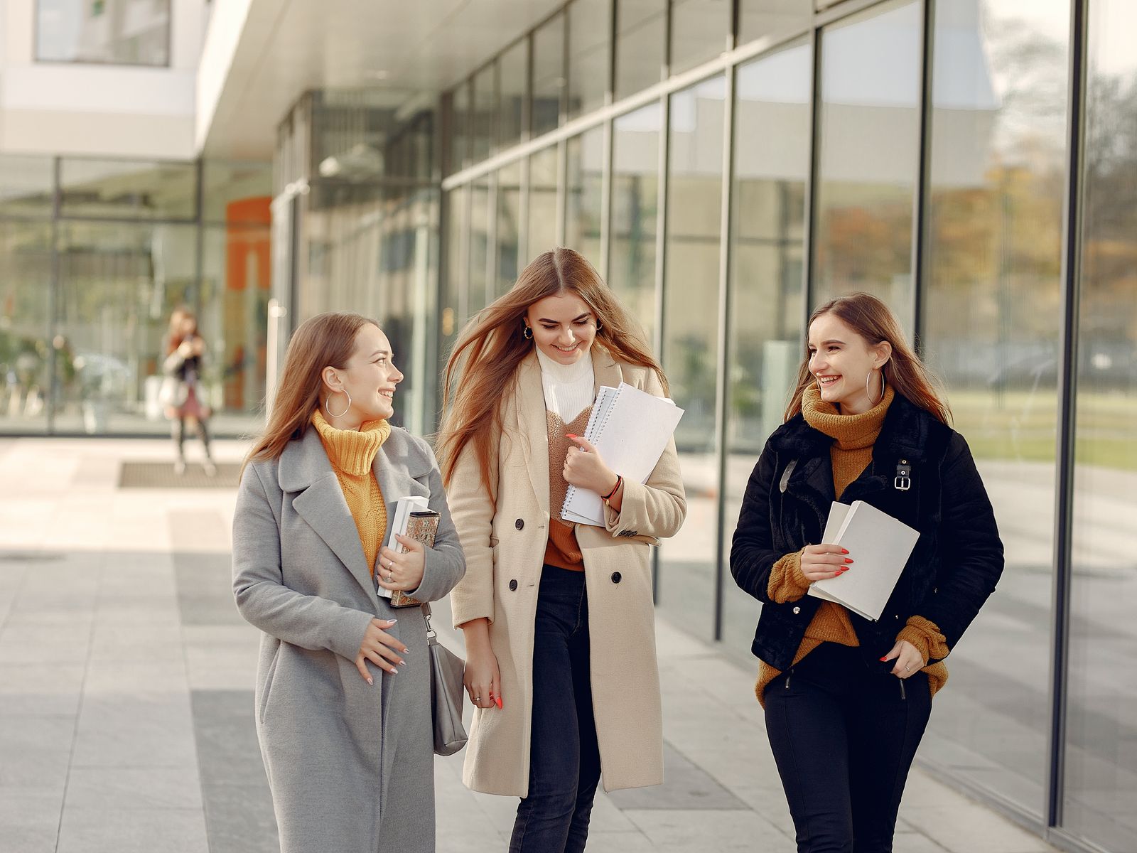 Three smiling students walking together with notebooks